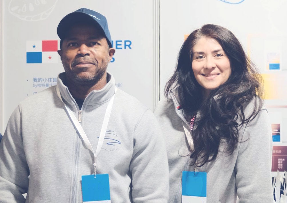Two people wearing matching gray jackets with blue name tags in front of a colorful wall.